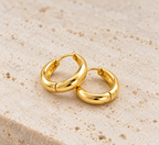 DUGO chunky huggie hoop earrings in polished gold with a smooth minimalist rounded design on a textured stone surface