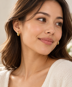 DUGO chunky huggie hoop earrings in polished gold worn by a woman with wavy brown hair and a white sweater