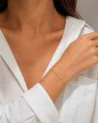 DUGO dainty gold curb chain bracelet worn on a woman's wrist with a white shirt, minimalist waterproof jewelry.