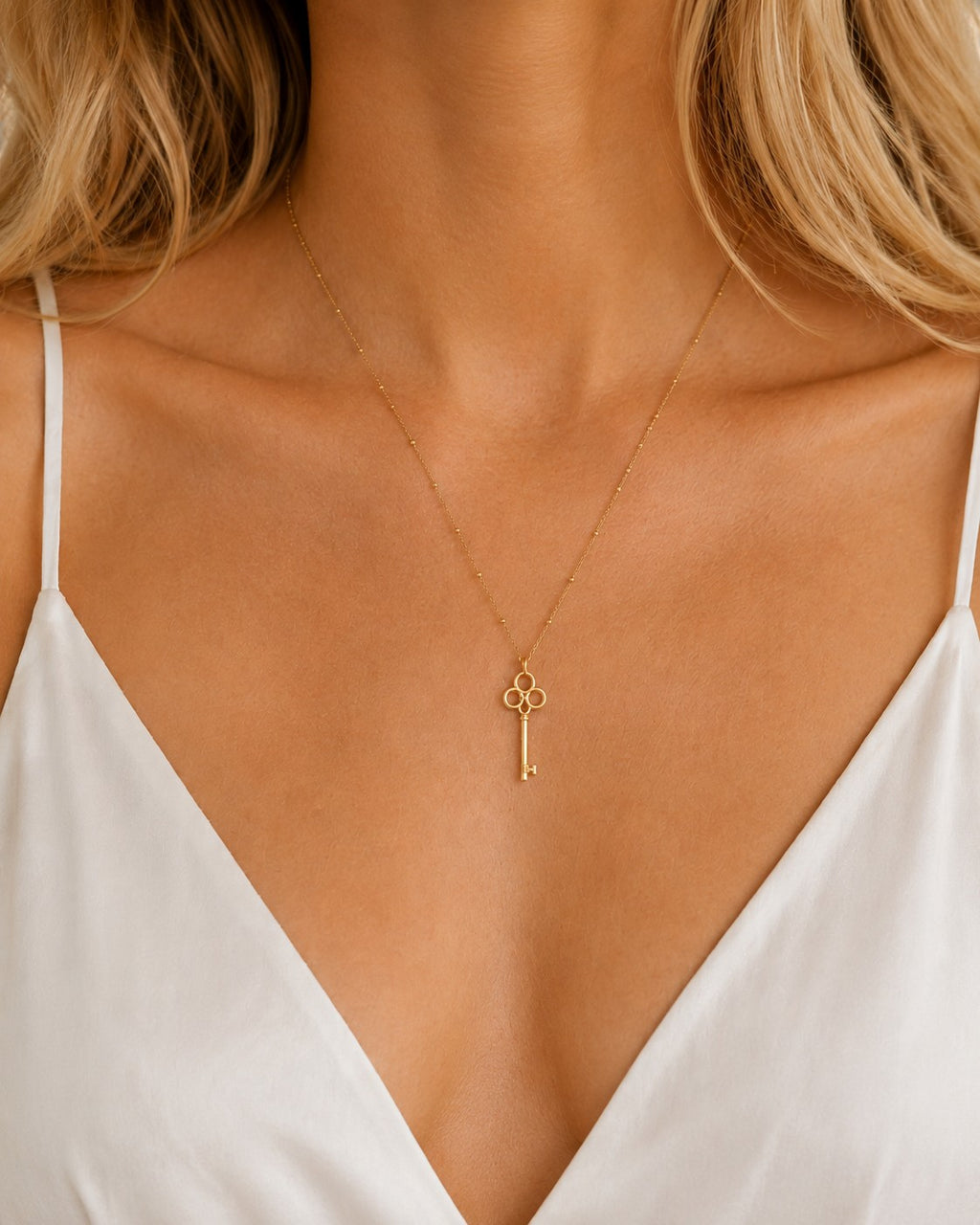 DUGO 18K gold filled vintage key pendant necklace on a dainty beaded ball chain worn by a woman in a white top