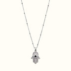 DUGO silver hamsa hand necklace with cubic zirconia stones and a black evil eye center on a delicate beaded chain.