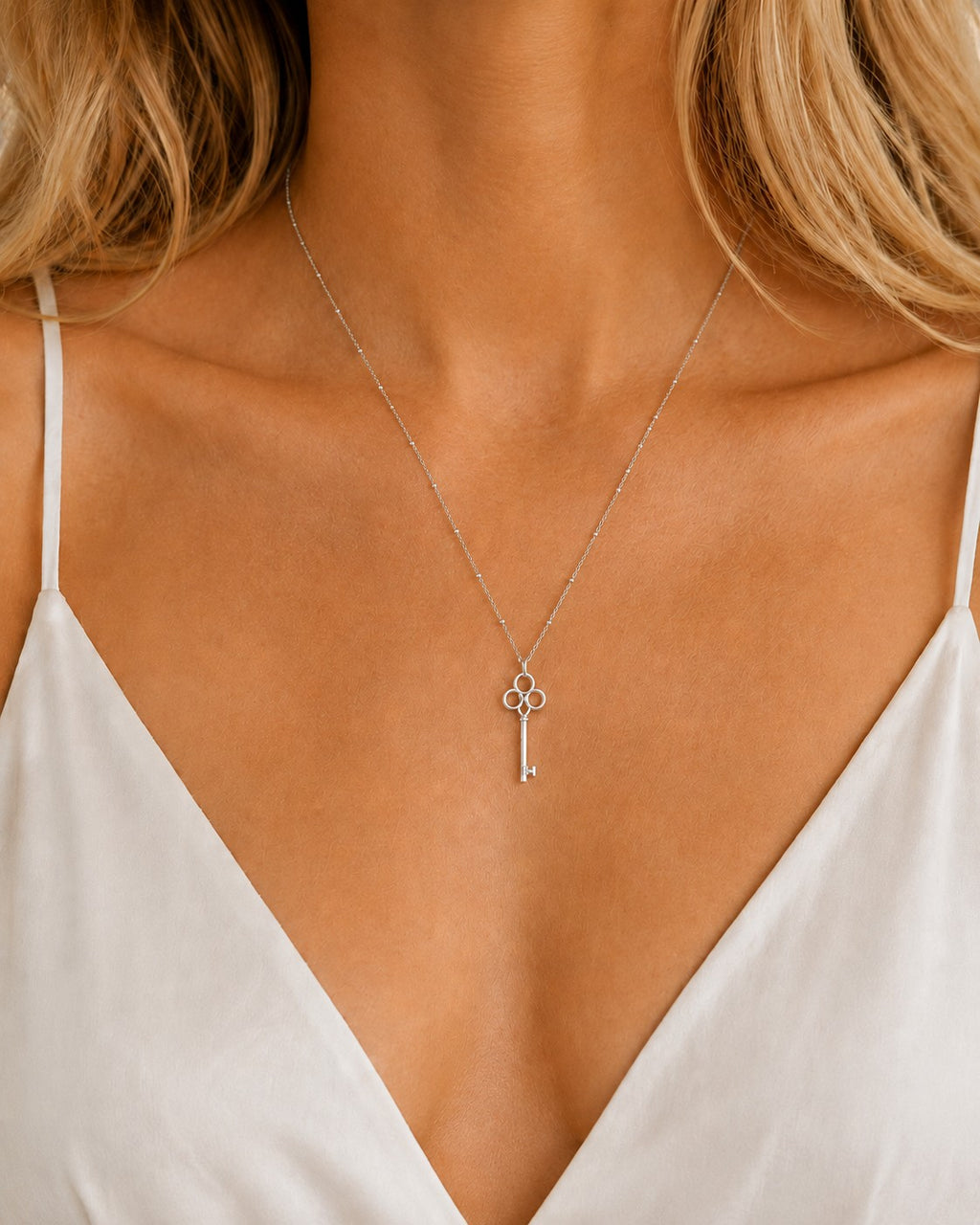 DUGO silver vintage key pendant on a dainty beaded ball chain worn by a woman in a white camisole