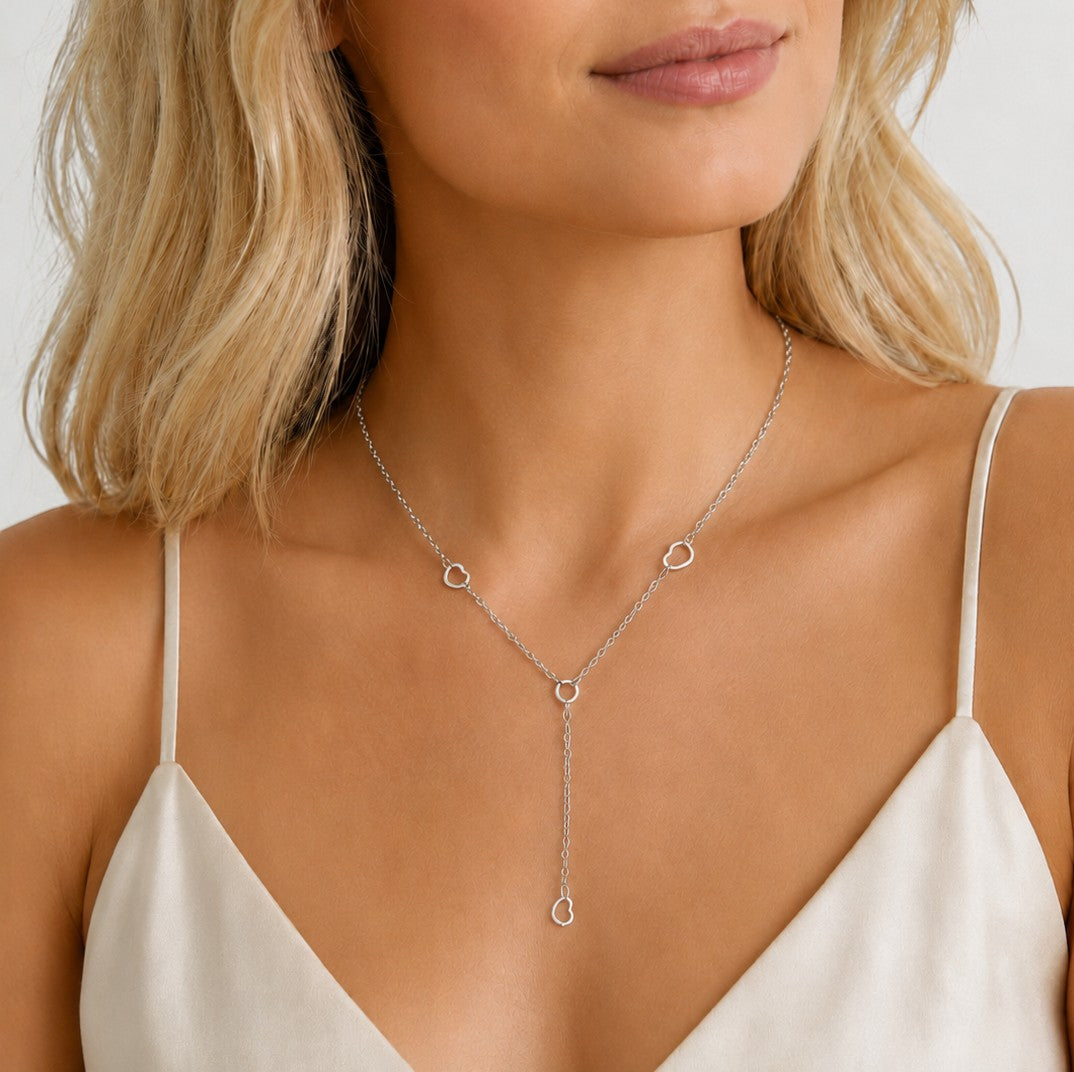 DUGO silver lariat heart necklace worn by a woman in a white camisole, featuring delicate heart charms.