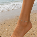 DUGO delicate multicolor beaded anklet on a woman's ankle at the beach with soft sand and ocean waves in background
